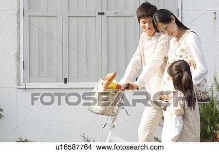Mother, father and daughter walking with groceries in bicycle basket View Large Photo Image Picture - Mother, father and daughter walking with groceries in bicycle basket. Fotosearch