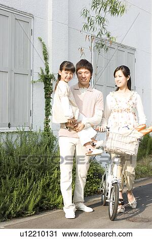 Stock Image - Mother, father and daughter walking with groceries in bicycle basket. Fotosearch