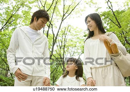 Stock Image - Mother, father and daughter walking through park. Fotosearch