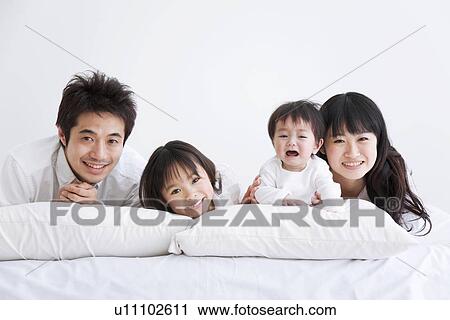 Stock Image - Mother, father daughter and crying baby son lying on bed. Fotosearch