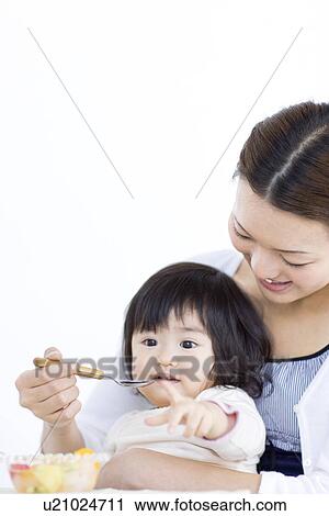 Stock Image - Mother feeding baby daughter fruit salad. Fotosearch