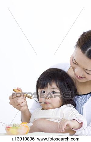 Stock Photograph - Mother feeding baby daughter fruit salad. Fotosearch