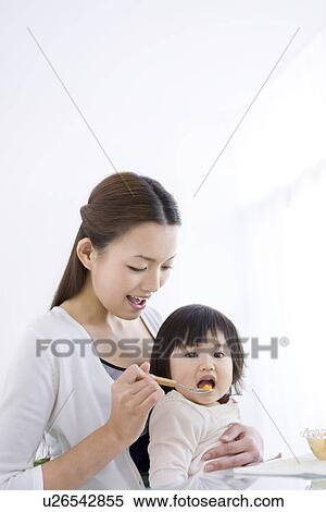 Stock Photography - Mother feeding baby daughter fruit salad. Fotosearch