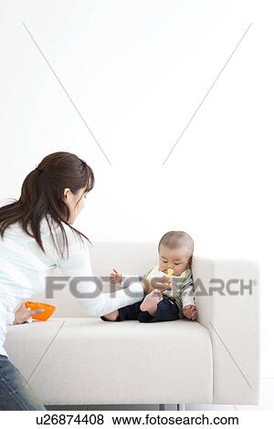 Stock Photo - Mother feeding her baby on the couch. Fotosearch