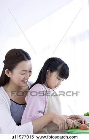 Stock Photography - Mother helping daughter to slice tomatoes. Fotosearch