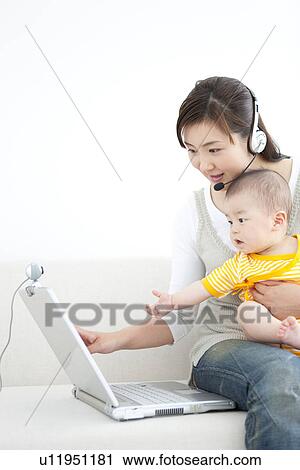 Stock Image - Mother holding her baby and using laptop. Fotosearch