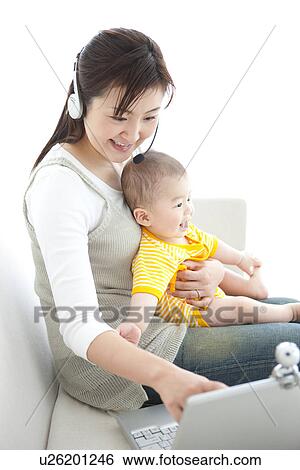 Stock Photograph - Mother holding her baby and using laptop. Fotosearch
