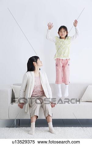 Stock Photography - Mother sitting on couch watching daughter jump up and down. Fotosearch