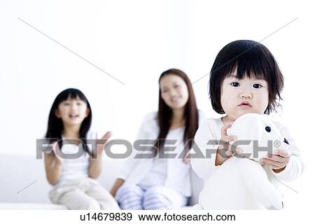 Stock Photo - One year old girl holding teddy with mother and sister in the background. Fotosearch
