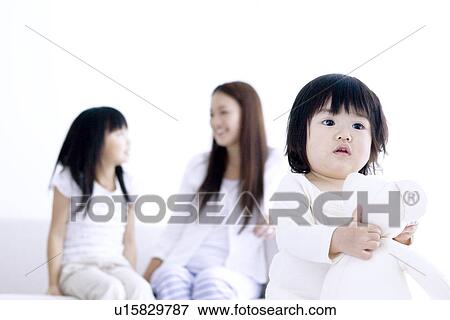 Stock Photo - One year old girl holding teddy with mother and sister in the background. Fotosearch