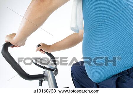 Stock Image - Overweight man exercising on a gym machine. Fotosearch