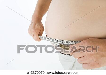 Stock Image - Overweight man measuring his pot belly. Fotosearch
