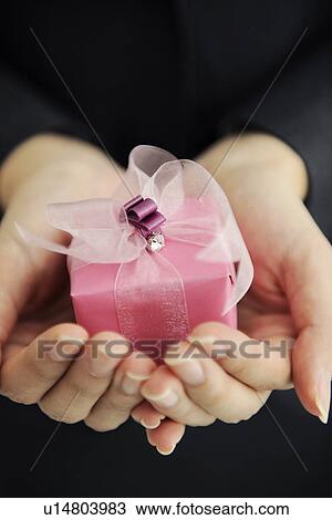 Stock Image - Person holding pink gift box. Fotosearch