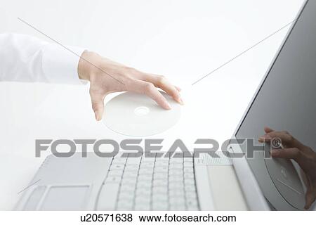 Stock Photo - Person inserting compact disc into laptop. Fotosearch