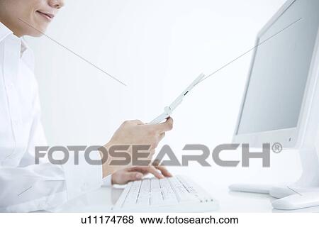 Stock Photo - Person using mobile phone next to computer. Fotosearch