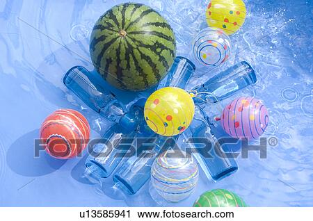 Stock Image - Plastic bottles, balls and balloons and a watermelon floating in a paddling pool. Fotosearch