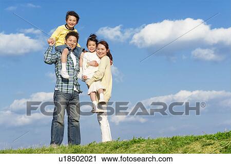 Stock Image - Portrait of a family of four at the park against a blue sky. Fotosearch