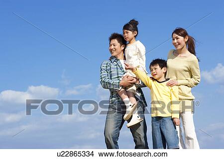 Picture - Portrait of a family of four looking into the distance against a blue sky. Fotosearch