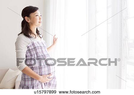 Stock Photo - Portrait of pregnant woman standing by a window. Fotosearch