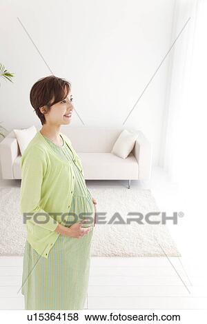 Portrait of pregnant woman standing in her living room View Large Photo Image Stock Photo - Portrait of pregnant woman standing in her living room. Fotosearch