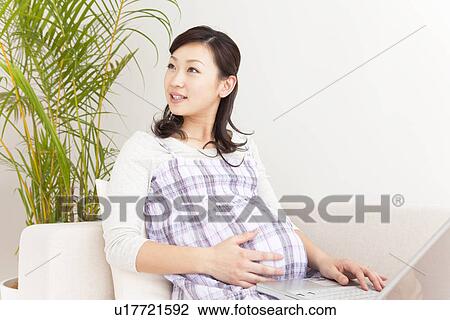 Pregnant woman sitting on sofa using laptop View Large Photo Image Stock Image - Pregnant woman sitting on sofa using laptop. Fotosearch