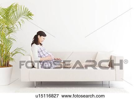 Stock Photo - Pregnant woman sitting on sofa using laptop. Fotosearch