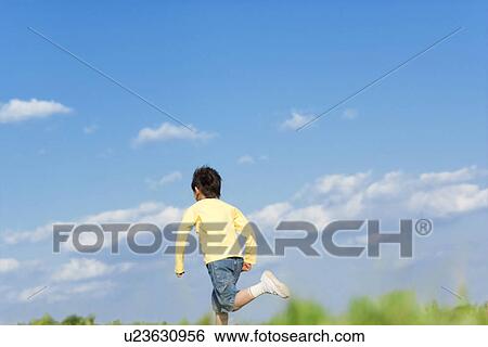 Stock Photograph - Rear view of young boy running against a blue sky. Fotosearch