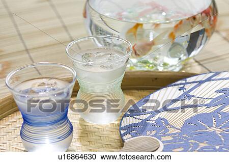 Stock Image - Saki cups on a tray next to a Japanese fan with a fishbowl in the background. Fotosearch