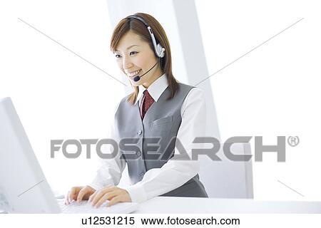 Stock Photography - Smiling businesswoman wearing headset and typing on computer. Fotosearch