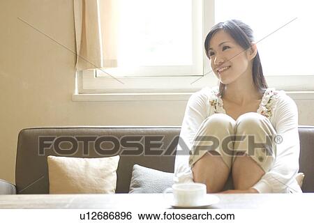 Stock Photograph - Smiling young woman sitting on sofa. Fotosearch
