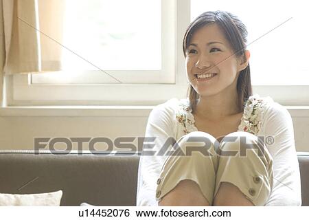 Stock Photograph - Smiling young woman sitting on sofa. Fotosearch