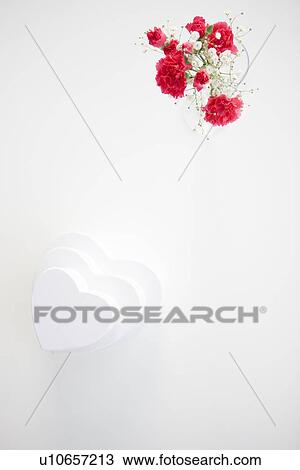 Stock Image - Stack of heart shaped gift boxes and a vase of carnations and baby's breath. Fotosearch