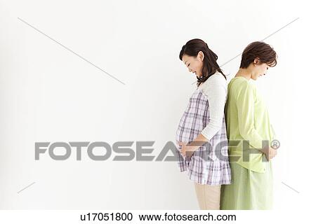 Stock Image - Studio portrait of two pregnant women standing back to back. Fotosearch