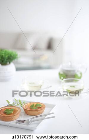 Stock Image - Tarts and herbal tea on a living room table. Fotosearch