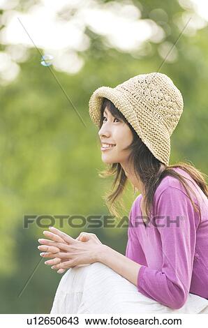 Stock Image - Woman crouching in a field with bubbles floating around her. Fotosearch