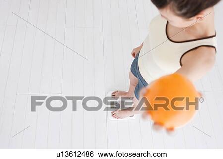 Woman holding an orange and weighing herself on bathroom scales View Large Photo Image Stock Photograph - Woman holding an orange and weighing herself on bathroom scales. Fotosearch