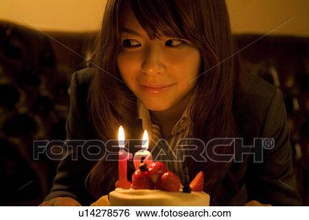 Stock Photograph - Woman leaning over to blow out the candles on her birthday cake. Fotosearch
