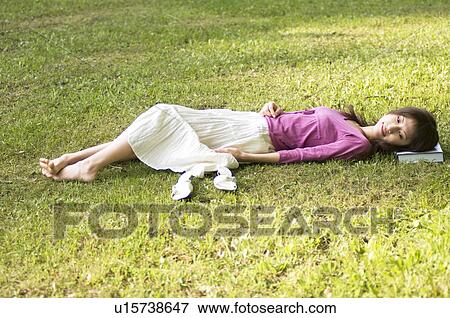 Woman lying in a field using a book as a pillow View Large Photo Image Stock Photo - Woman lying in a field using a book as a pillow. Fotosearch