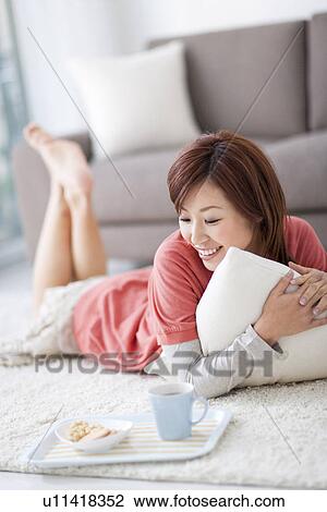 Stock Image - Woman lying on floor with coffee cup and cookies. Fotosearch