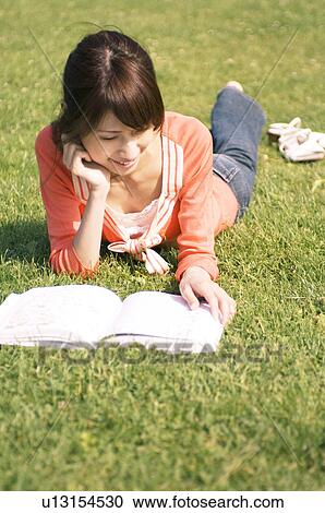 Woman lying on grass reading a book View Large Photo Image Stock Image - Woman lying on grass reading a book. Fotosearch