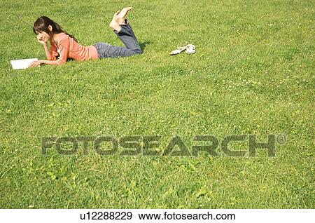 Woman lying on grass reading a book View Large Photo Image Stock Photo - Woman lying on grass reading a book. Fotosearch