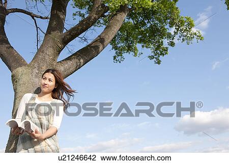 Woman reading a book next to a tree View Large Photo Image Stock Image - Woman reading a book next to a tree. Fotosearch