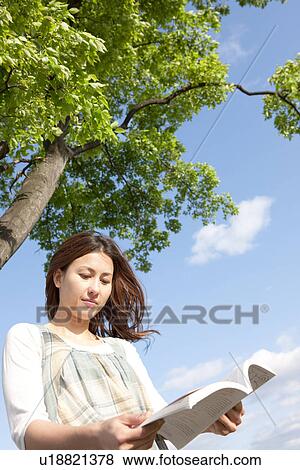 Stock Photo - Woman reading a book next to a tree. Fotosearch