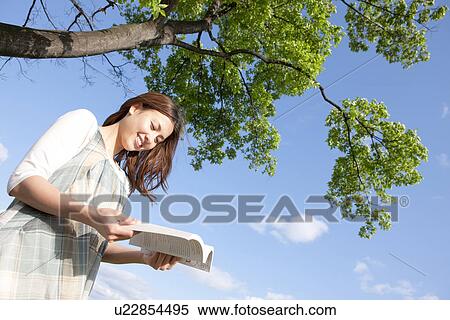 Woman reading a book next to a tree View Large Photo Image Stock Photography - Woman reading a book next to a tree. Fotosearch