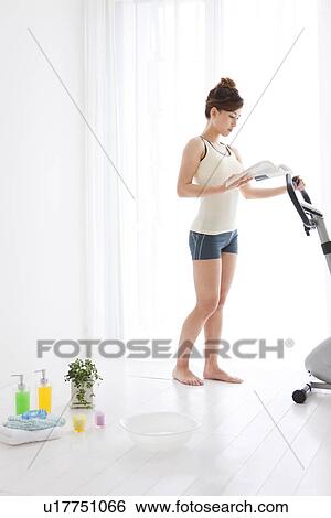 Stock Photograph - Woman reading a book next to an exercise bike. Fotosearch