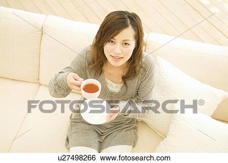 Stock Photograph - Woman sitting on sofa drinking tea. Fotosearch
