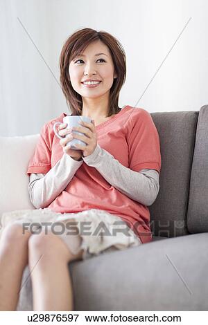 Stock Photo - Woman sitting on sofa holding coffee cup. Fotosearch