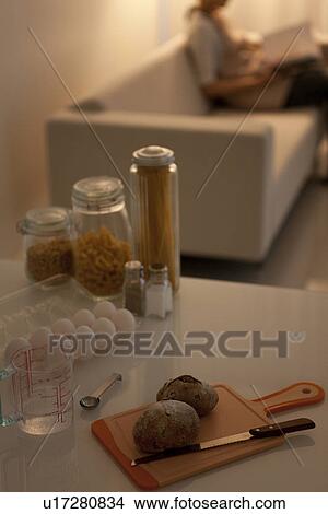 Woman sitting on sofa with ingredients on kitchen counter View Large Photo Image Picture - Woman sitting on sofa with ingredients on kitchen counter. Fotosearch