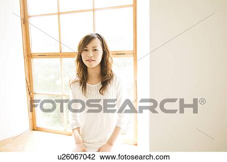 Stock Image - Woman sitting on window seat. Fotosearch