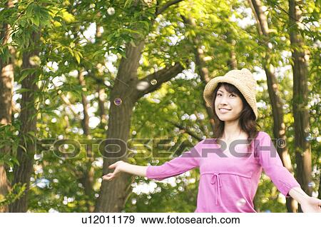 Stock Photo - Woman standing in a field with bubbles floating around her. Fotosearch